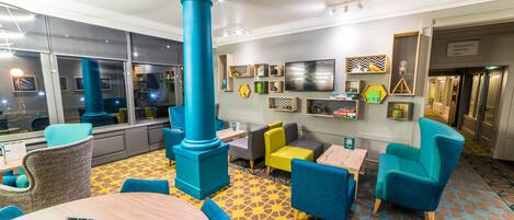 A modern lounge area with a large blue pillar, comfortable seating, and a patterned floor.