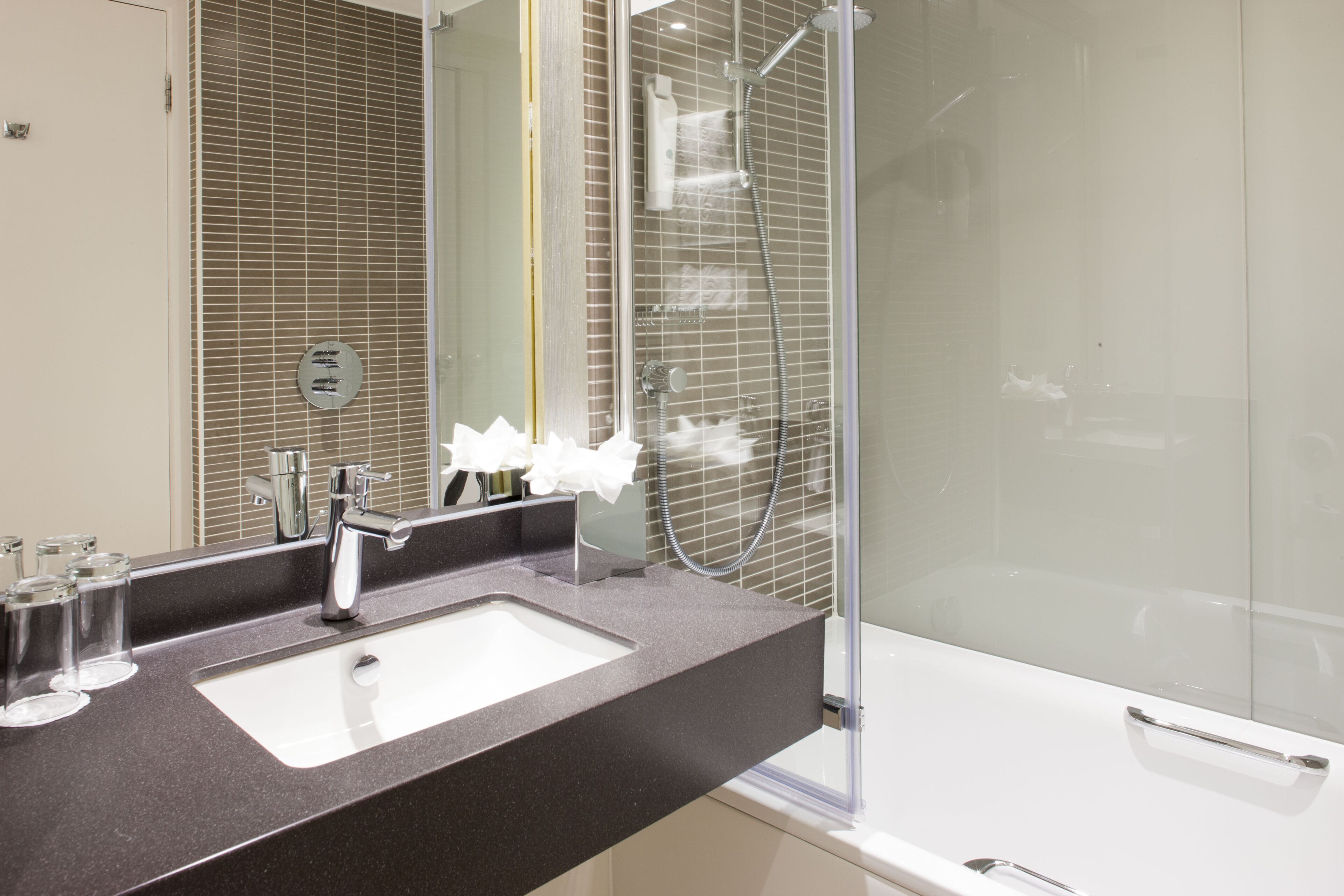 A modern bathroom with a large mirror, a sink, and a glass-enclosed shower.