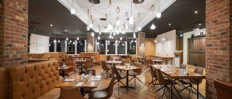 A restaurant with brick walls, wooden tables, and leather booths.
