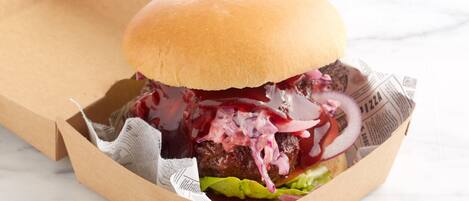 A burger in a paper container with lettuce, red onion, and a sauce.