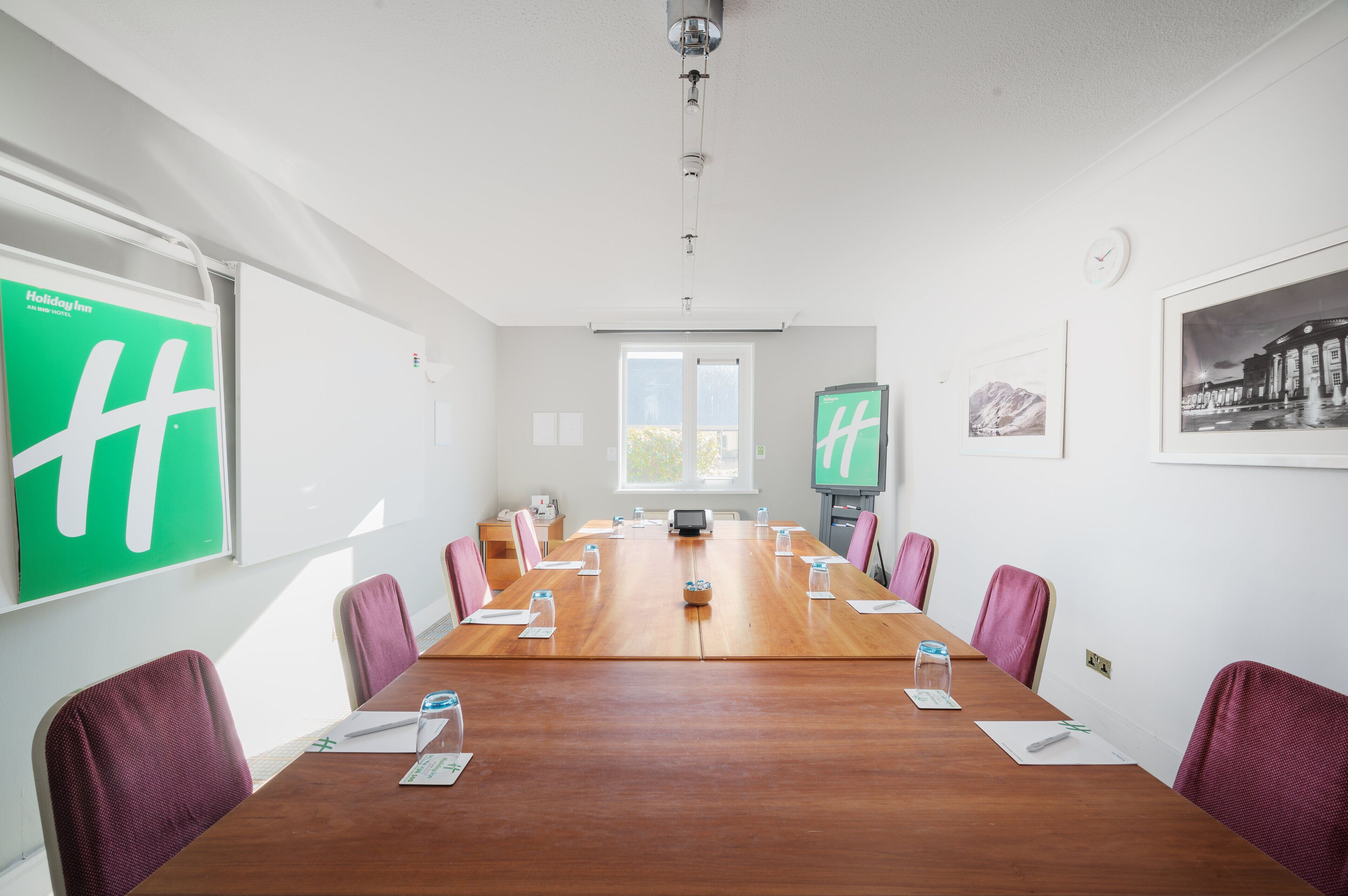 A conference room with a long wooden table, purple chairs, a projector screen, and a clock on the wall.