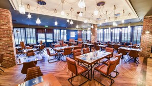 A spacious dining area with multiple tables and chairs, large windows, and hanging light fixtures. - Holiday Inn Brighouse by IHG (Brighouse)