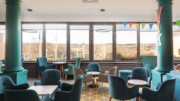 Relax in a spacious seating area with comfortable chairs and tables, offering a view of the outdoors.