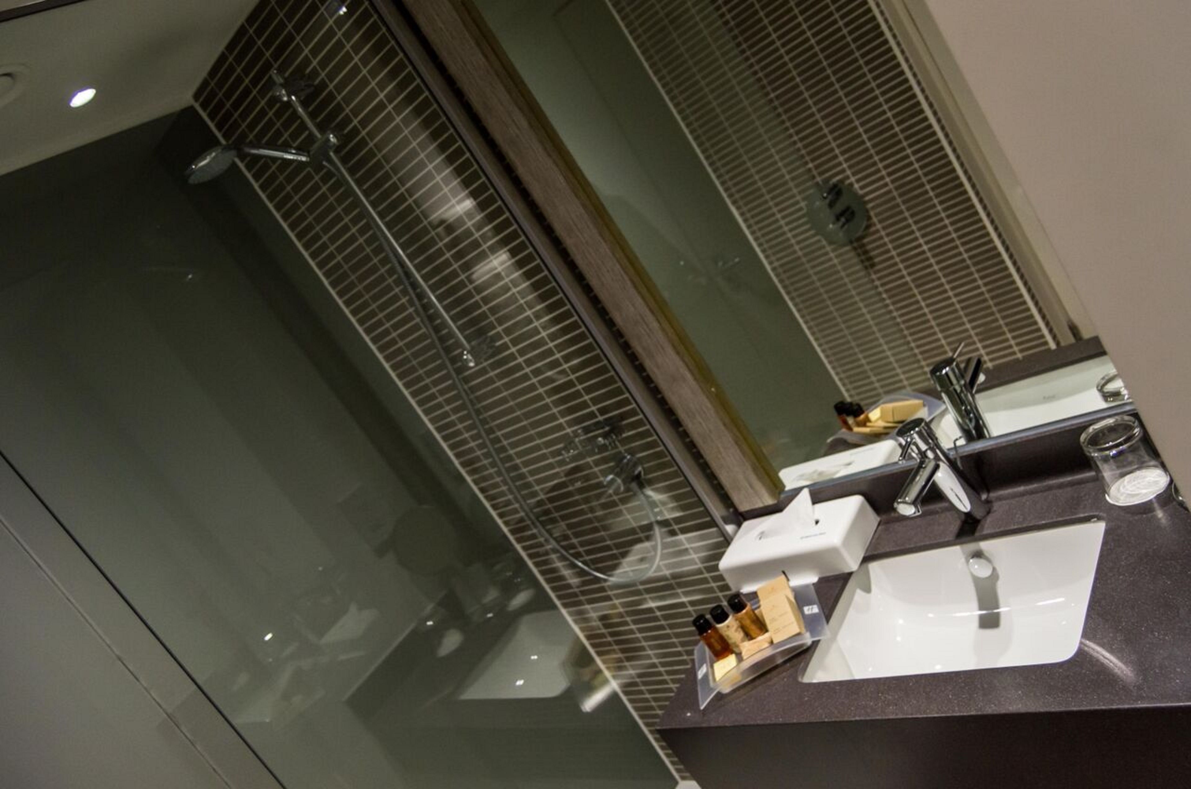 Een moderne badkamer met een glazen douchecabine, een witte wastafel met spiegel en toiletartikelen op het aanrecht.