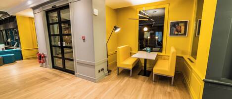 A reception area with a wooden floor, a blue sofa, a table with chairs, a fire exit sign, and a fire extinguisher.