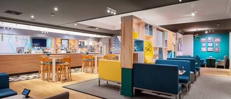 Un hall d’hôtel moderne comprenant un comptoir d’accueil, un espace salon et un espace de jeux pour enfants.