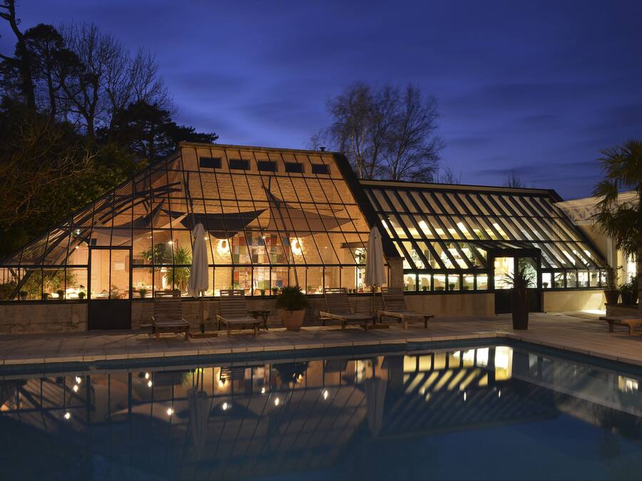 A modern building with a glass facade, a pool, and outdoor seating.