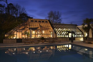 Un edificio moderno con fachada de vidrio, piscina y mobiliario exterior.