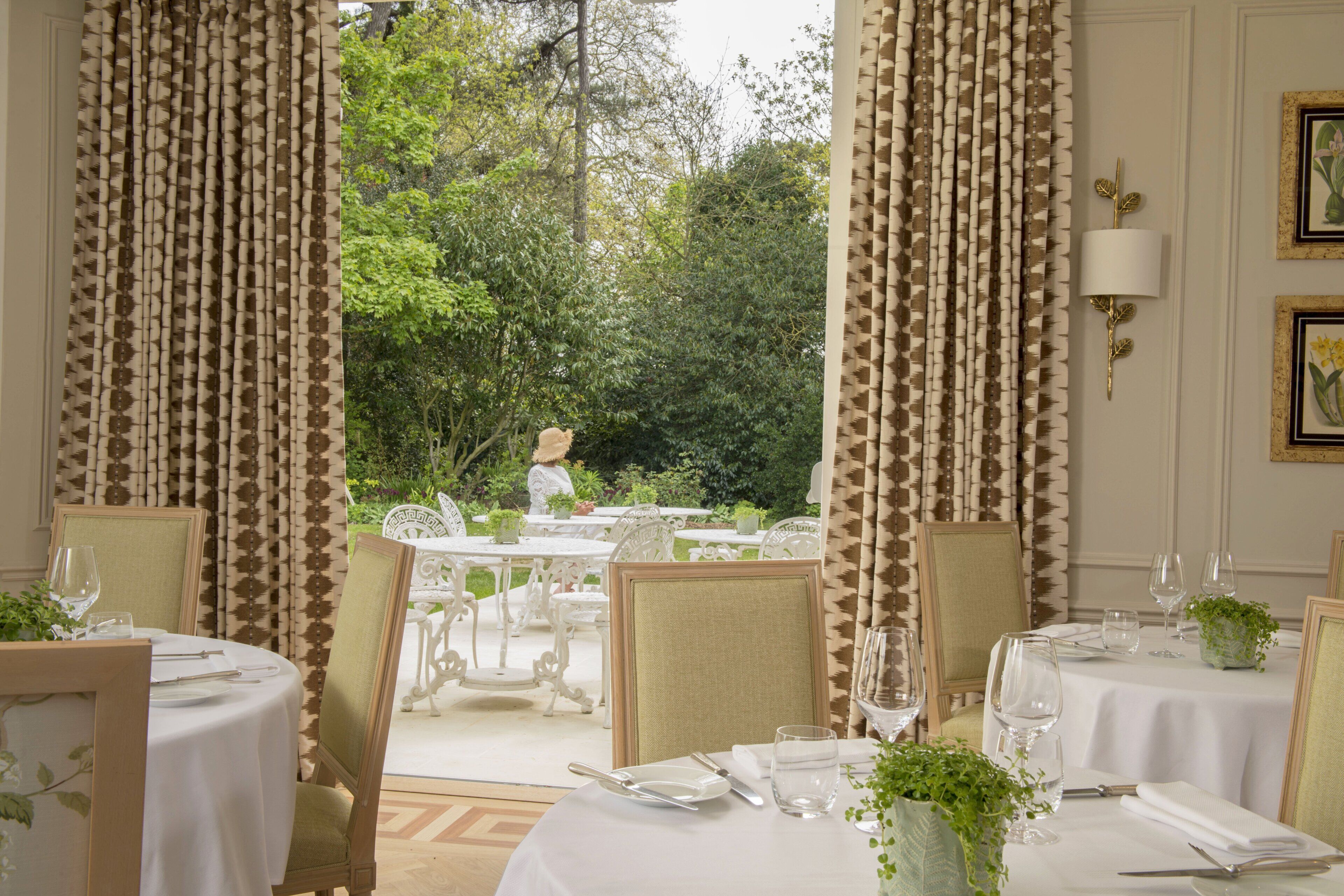 A dining area with tables set for two, white tablecloths, and chairs.