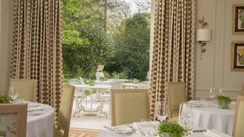 A dining area with tables set for two, white tablecloths, and chairs.