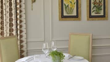Une table à manger est dressée avec une nappe blanche, de la verrerie et un centre de table. Des reproductions botaniques encadrées ornent le mur, ainsi qu’une lampe fixée au mur.
