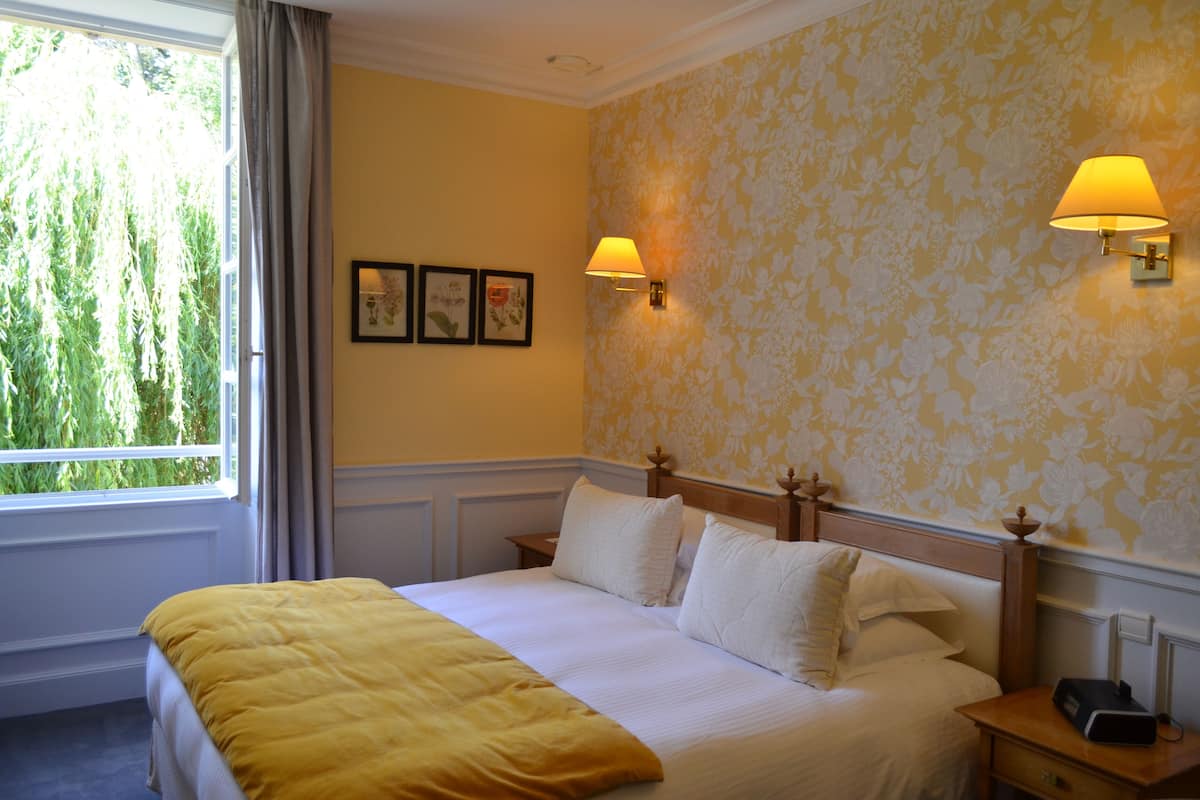 Una habitación de hotel con cama, dos mesitas de noche, una ventana con cortinas y lámparas fijadas a la pared.