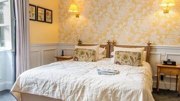 A neatly made bed with a quilt, two bedside tables with lamps, and a floral wallpaper pattern.