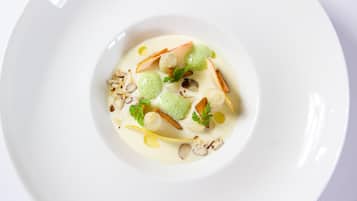 A white plate with a creamy dessert featuring green spheres, nuts, and a garnish.