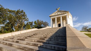 Uma escadaria imponente leva a um edifício clássico com uma estátua dourada de águia no topo.