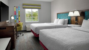 Quarto de hotel com duas camas, uma escrivaninha, televisão e janela com vista.