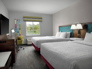 Quarto de hotel com duas camas, uma escrivaninha, televisão e janela com vista.