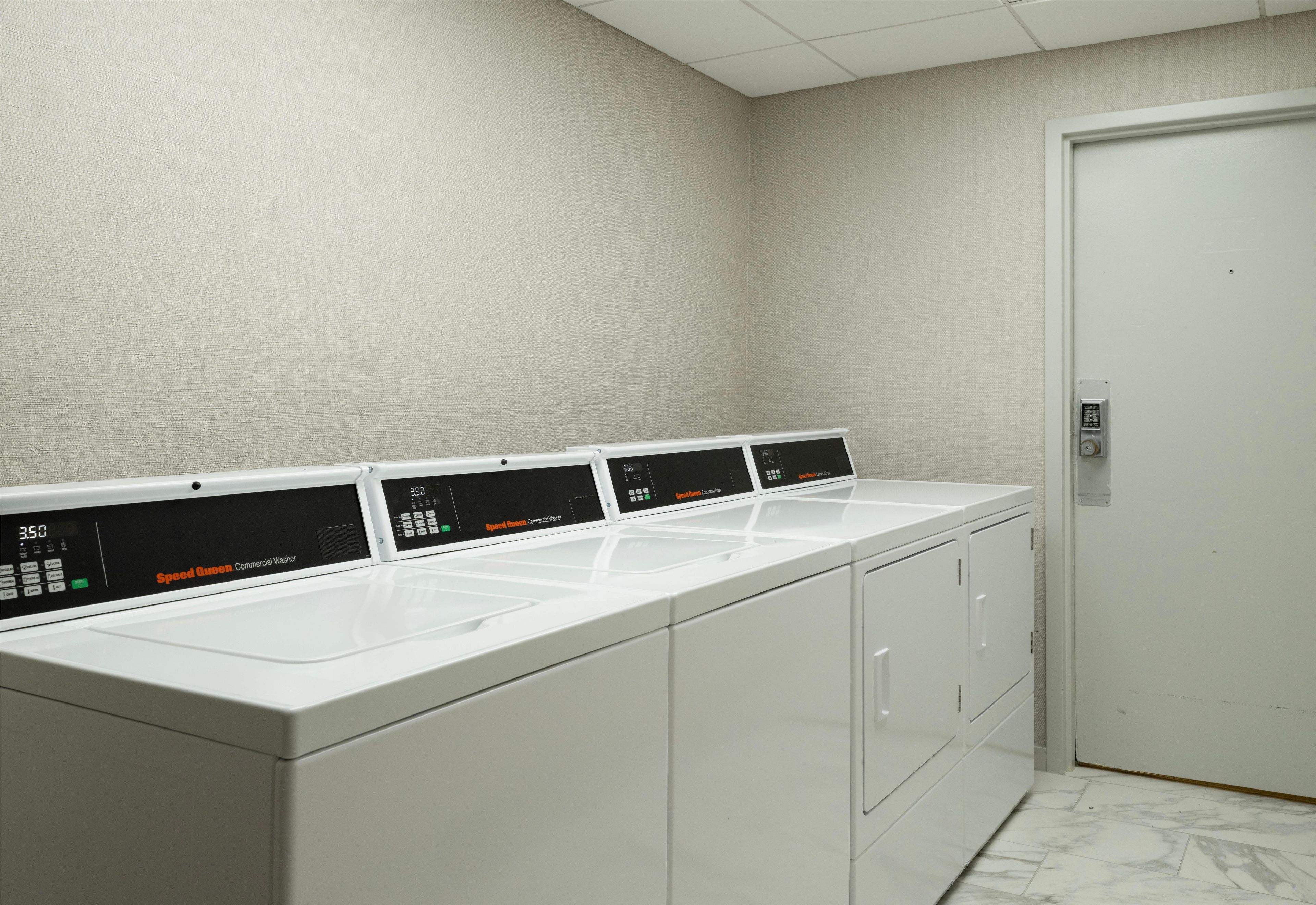 A row of Speed Queen commercial washers in a utility room with a white door and textured walls.