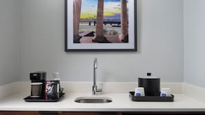 Uma cozinha com cafeteira, pia e quadro de uma ponte.