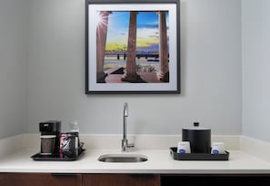 Uma cozinha com cafeteira, pia e quadro de uma ponte.