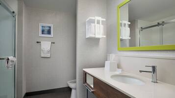 Un baño moderno con ducha de vidrio, un lavabo blanco y un espejo con marco verde.