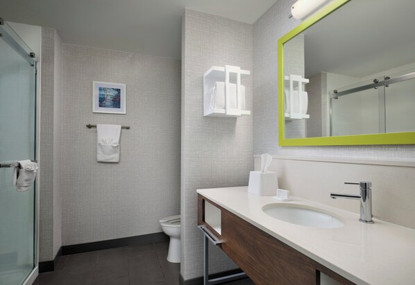 A modern bathroom with a glass shower, a white sink, and a mirror with a green frame.