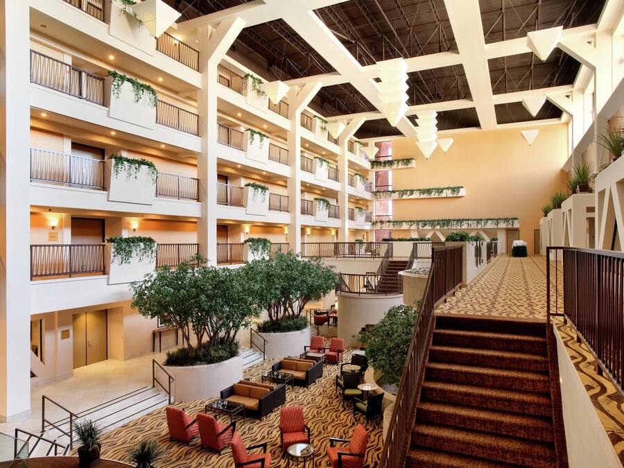 A multi-level hotel lobby with a central staircase, seating areas, and greenery.