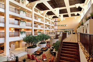 Un vestíbulo de hotel de varios niveles con una escalera central, zonas de estar y plantas.