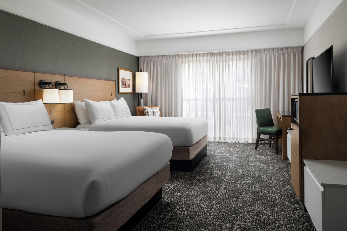 A hotel room with two beds, a desk, a chair, a television, and a window with curtains.