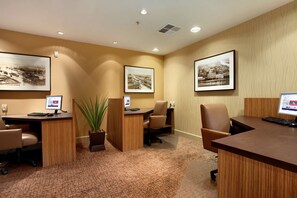 Un salón de conferencias con tres escritorios, cada uno con un ordenador y una silla. Hay cuadros en las paredes y una planta en maceta en el centro.
