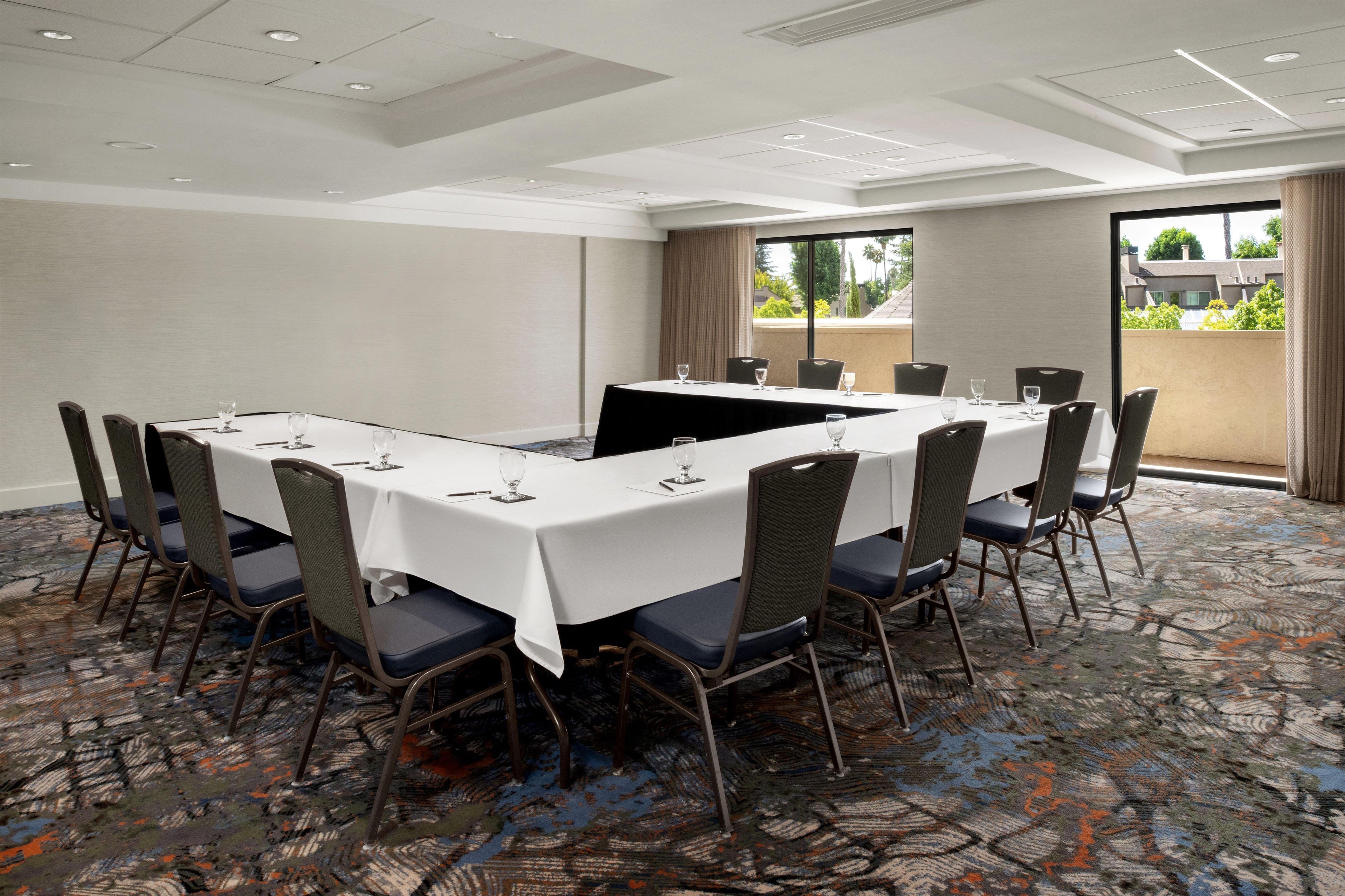 A conference room with a long table, chairs, and a view of buildings through a large window.