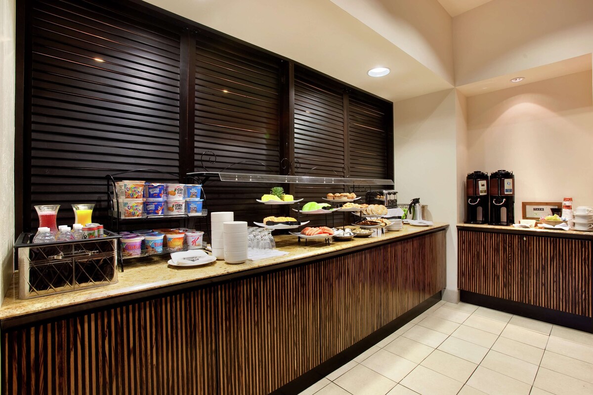 Mostrador de buffet con diversas opciones de comida, entre ellas frutas, verduras y bebidas.