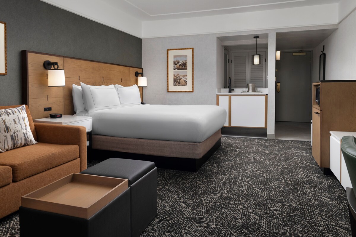 A hotel room with a bed, a sofa, a desk, a chair, and a small table.