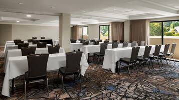 A conference room with multiple tables and chairs, large windows with curtains, and a patterned carpet.