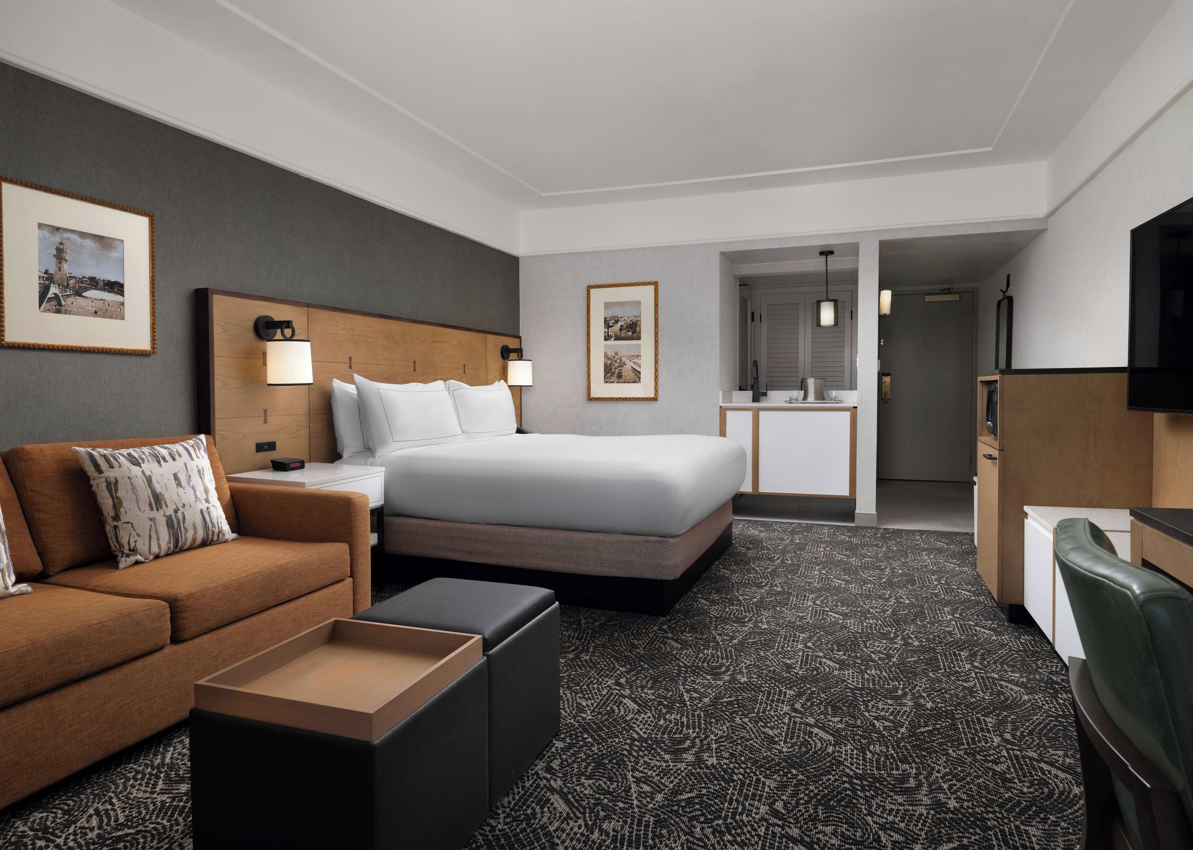 A hotel room with a bed, a sofa, a desk, a television, and a bathroom visible through an open door.
