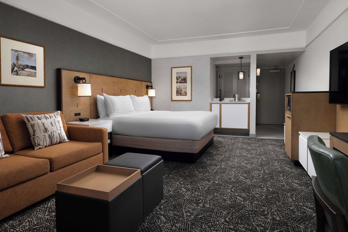 A hotel room with a bed, a sofa, a desk, and a TV.