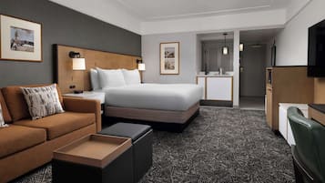 A hotel room with a bed, a sofa, a desk, a television, and a bathroom visible through an open door.