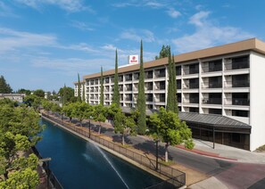 A multi-story hotel with a swimming pool and a landscaped walkway.