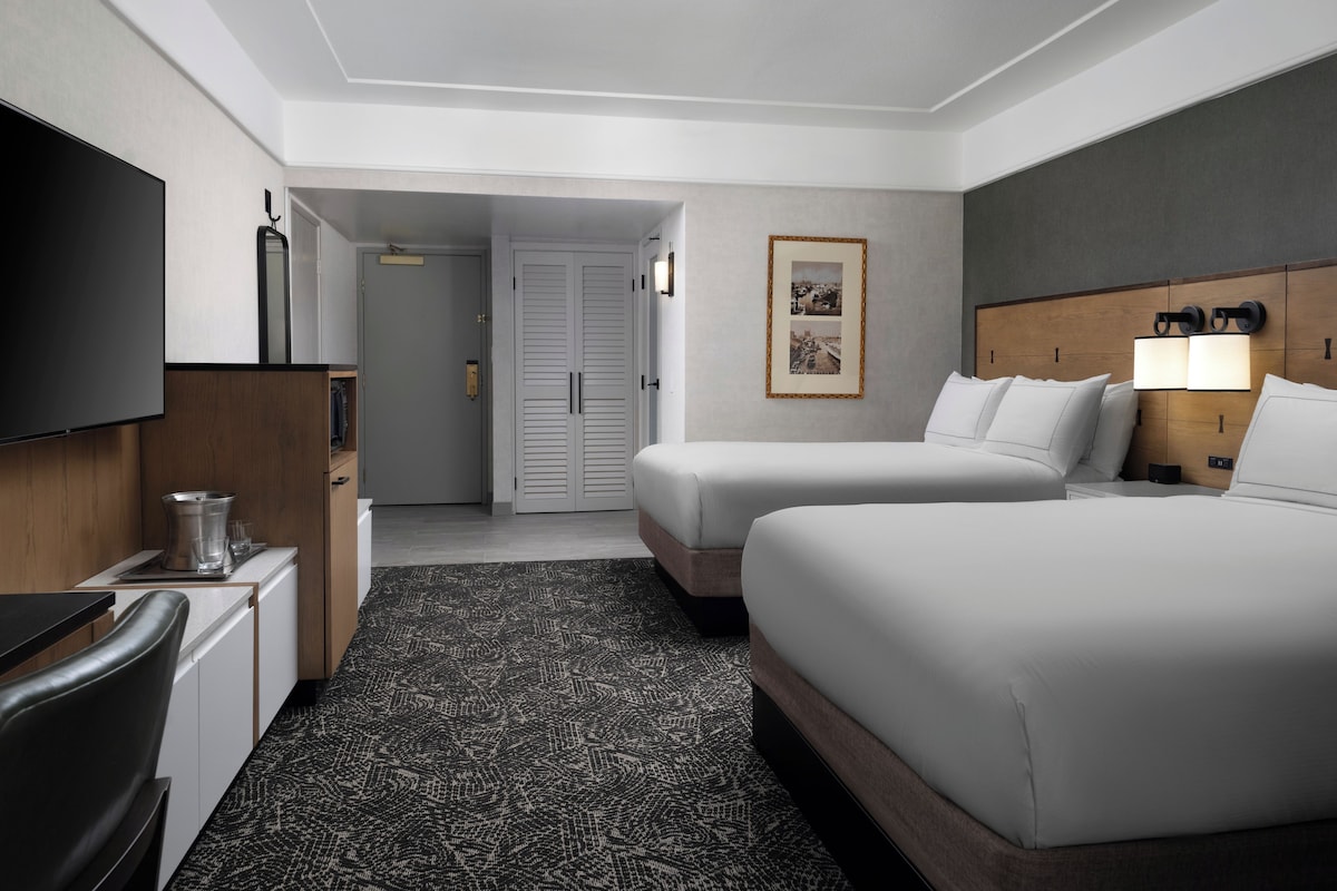 A hotel room with two beds, a TV, a desk, and a bathroom.