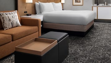 Habitación de hotel con cama, sofá, mesita de noche, lámpara, un cuadro en la pared y alfombra.