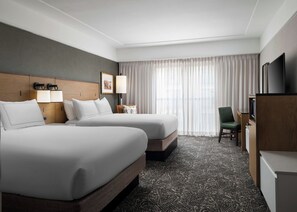 A hotel room with two beds, a desk, a chair, a television, and a window with curtains.