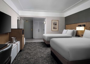 A hotel room with two beds, a TV, a minibar, and a door leading to a hallway.