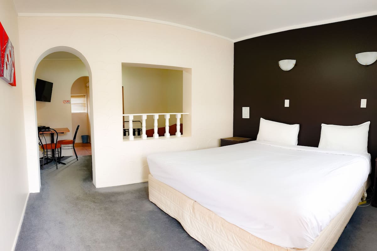 Ein Hotelzimmer mit einem großen Bett, einem Schreibtisch mit Stuhl, einem Fernseher und einem durch einen Bogen sichtbaren Badezimmer.