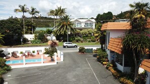 A parking lot with a pool area, a white building, and a car. - Casa Bella Motel (Paihia)