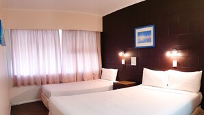 A hotel room with two beds, a large window with curtains, a dark headboard, and wall-mounted lights. - Casa Bella Motel (Paihia)