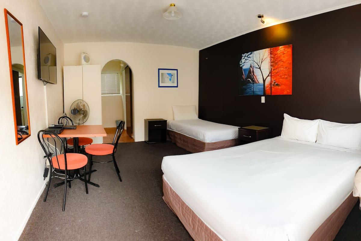 Ein Hotelzimmer mit einem großen Bett, einem Schreibtisch mit zwei Stühlen, einem kleinen Tisch und einem Einzelbett auf der anderen Seite.