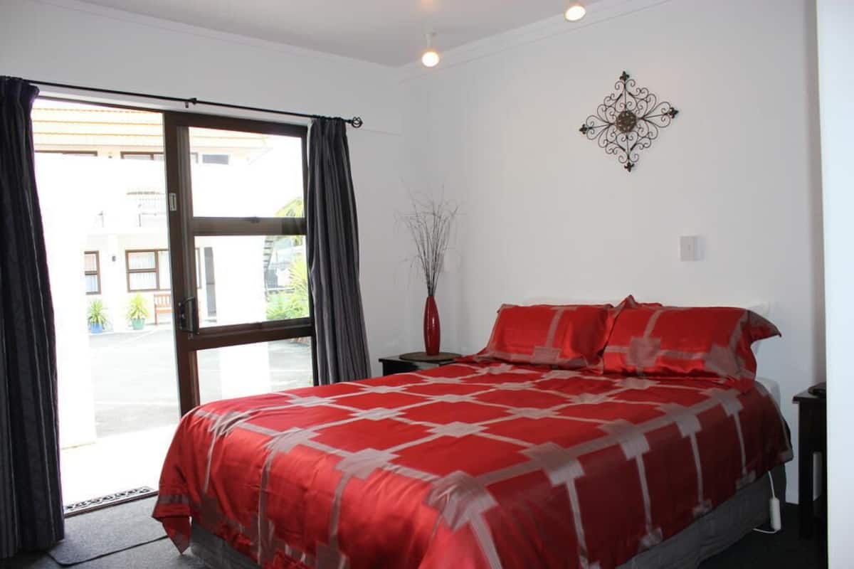 Ein Schlafzimmer mit einem großen Bett, einer Schiebetür, einem kleinen Tisch mit einer Vase und einem Wanddekor.