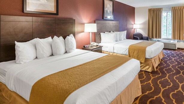 Hotelkamer met twee bedden, elk voorzien van witte lakens en een bruine sprei. Twee nachtkastjes met lampen, een raam met gordijnen en een ingelijst schilderij aan de muur.