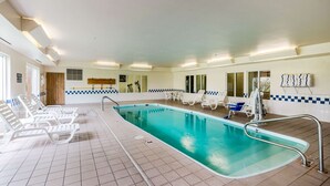Een binnenzwembad met betegelde vloer, ligbedden en een zwembadgedeelte met een balustrade.