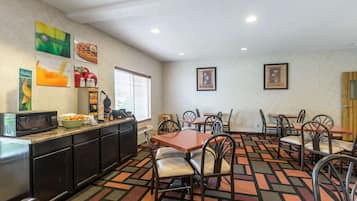 A dining area with tables and chairs, a microwave, and a fruit bowl on the counter.